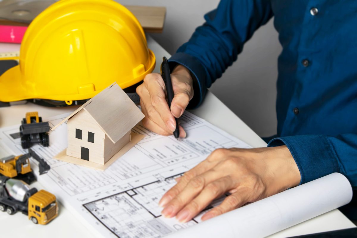 A construction specialist sitting in his office, a house model, safety helmet, and vehicle miniatures on the table, and preparing construction estimates.