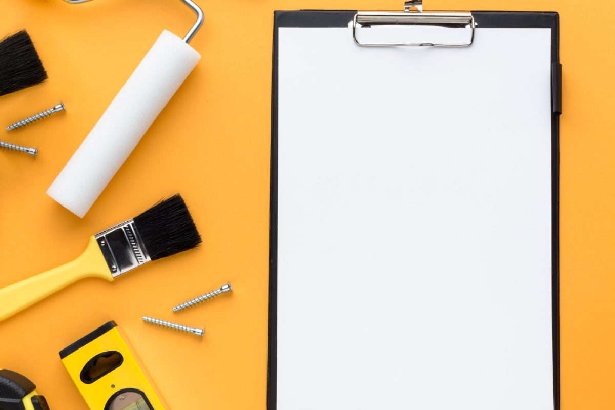 Tools and a blank clipboard on an orange background, ideal for preparing a drywall bid template or construction estimate.